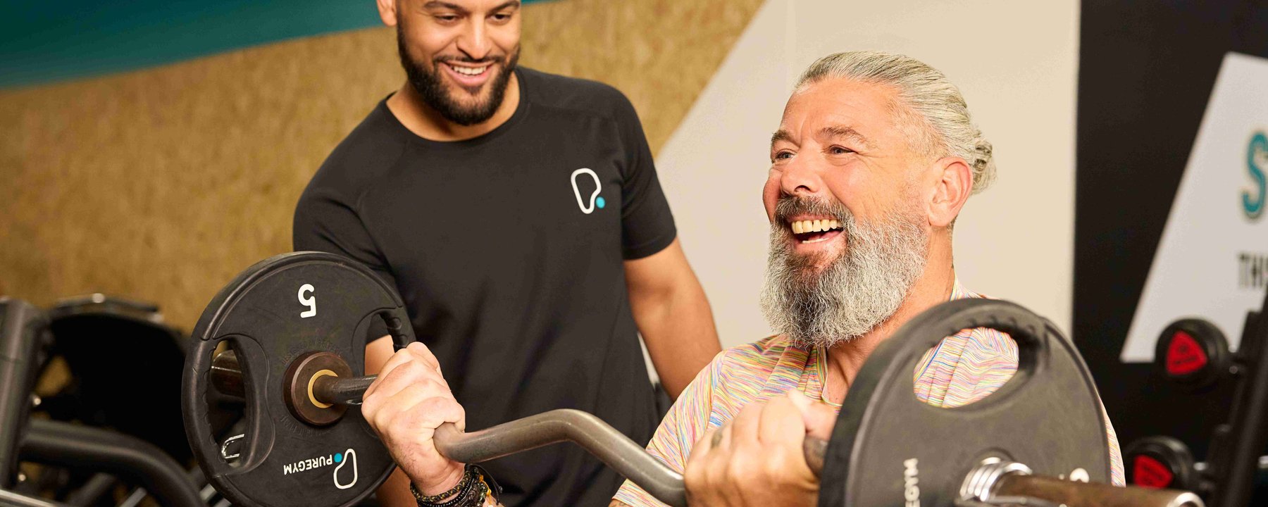 Man lifting barbell while trainer encourages him in gym setting