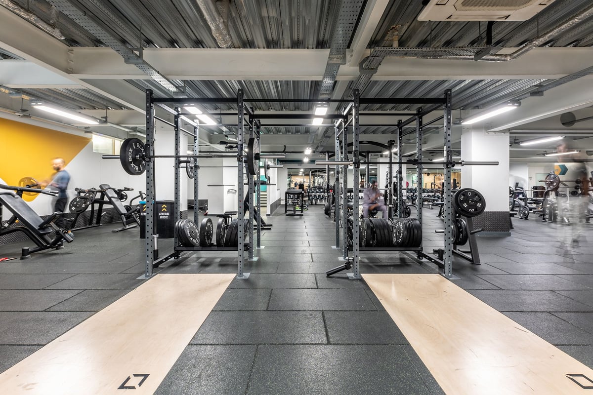 PureGym London Finsbury Park: Squat racks, weight plates, benches, rubberized flooring in a gym with industrial ceiling.