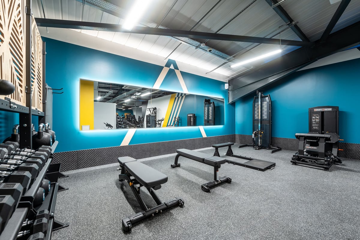 PureGym Letchworth: Gym studio with weight benches, freeweights, resistance bands, and bright teal accent walls.