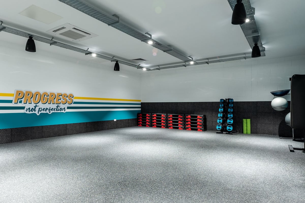 PureGym Alloa: Workout studio with weight plate rack, Progress branding, spotlights, and rubberized flooring.