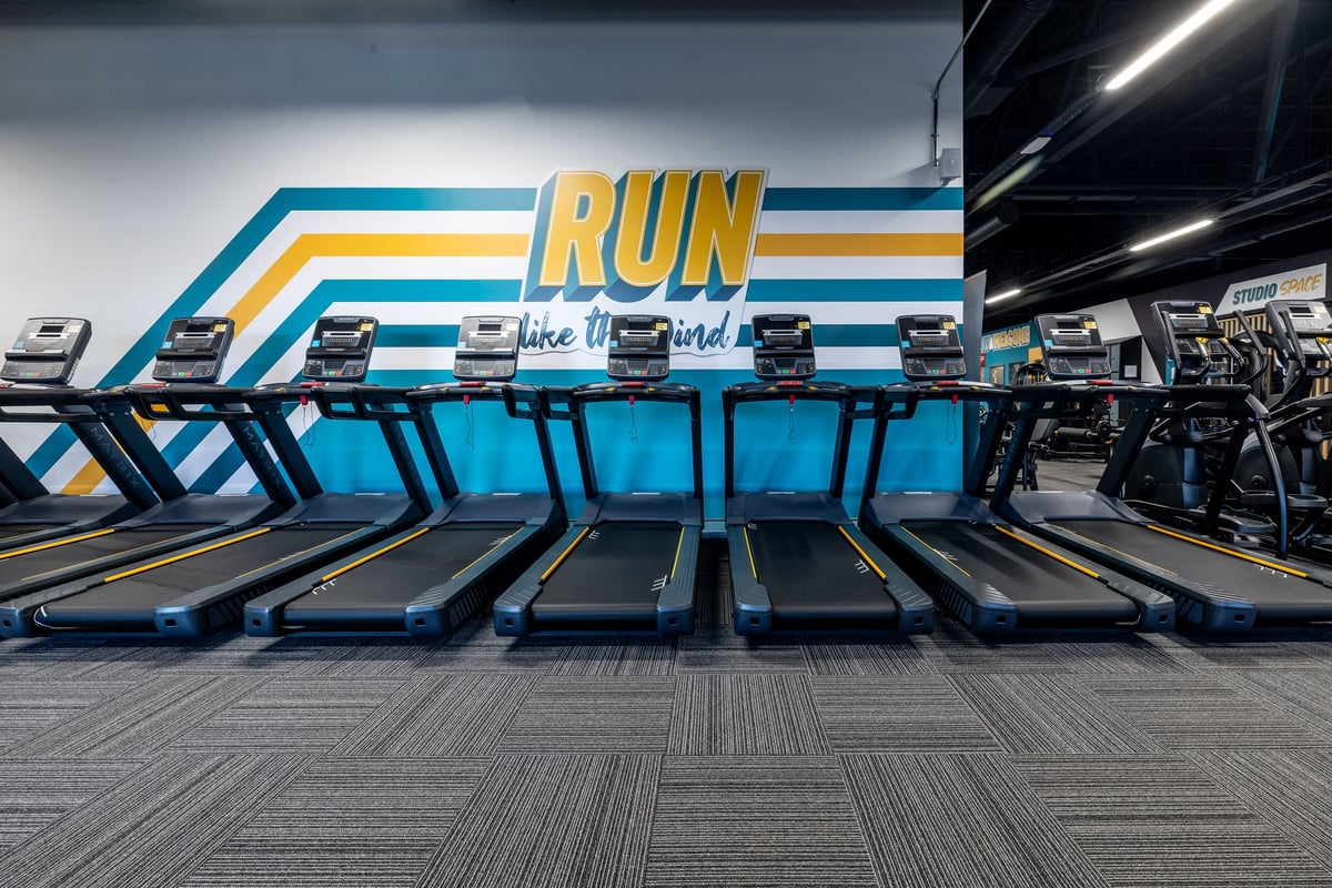 PureGym Hartlepool: Rows of treadmills with "RUN" sign and vibrant stripes in a fitness studio.