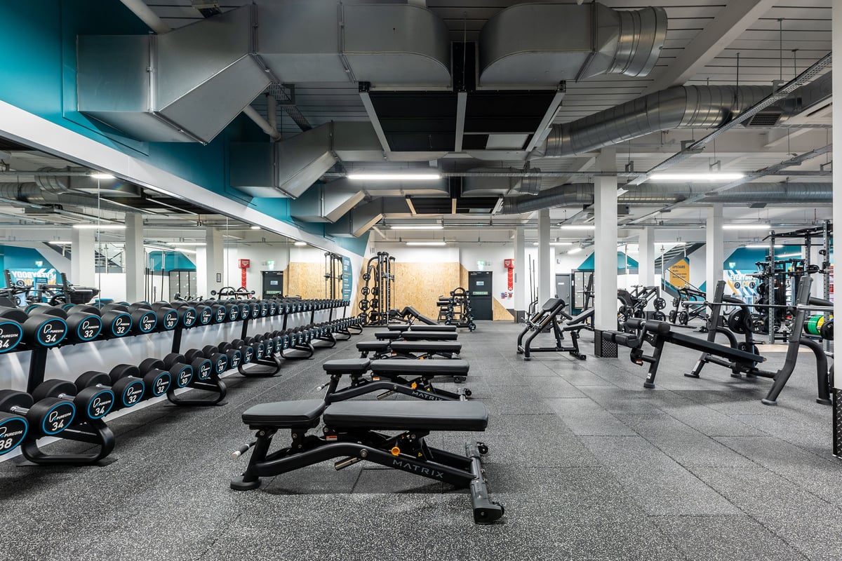 PureGym Glasgow Milngavie: Rows of weight benches, dumbbells, and exercise machines in an industrial-style gym interior.