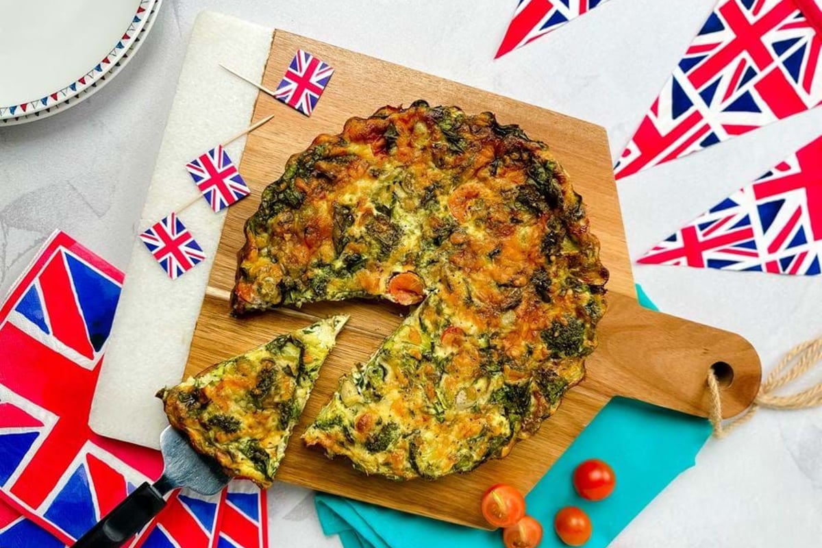 Vegetable quiche with a slice being served on a spatula on a wooden board.