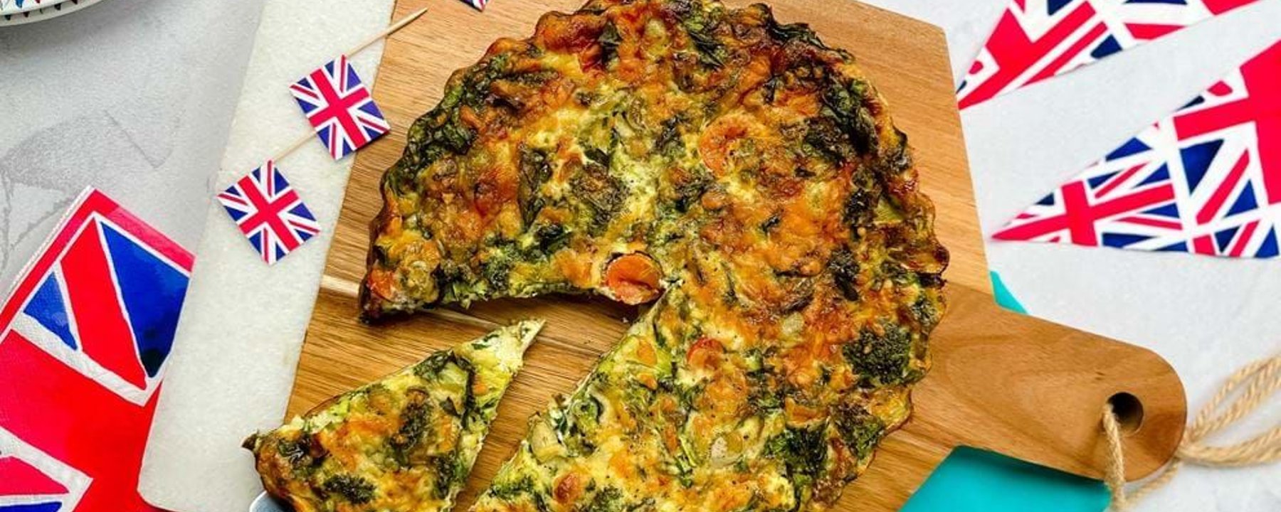 Vegetable quiche with a slice being served on a spatula on a wooden board.