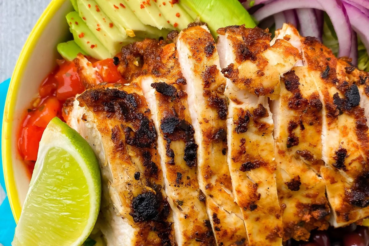 Grilled chicken slices with avocado, red onion, black beans, rice, lime wedge, and salsa