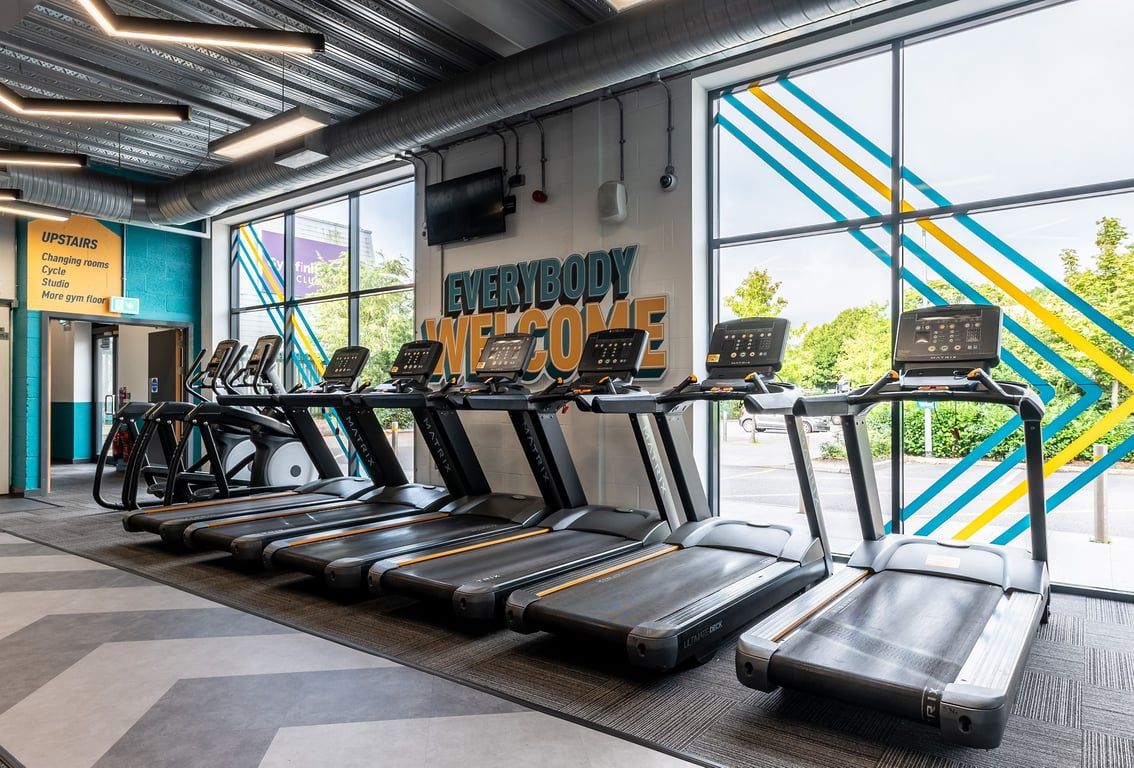 PureGym Reading Basingstoke Road: Rows of treadmills, vibrant geometric wall art, and signage saying "Everybody Fit Out".
