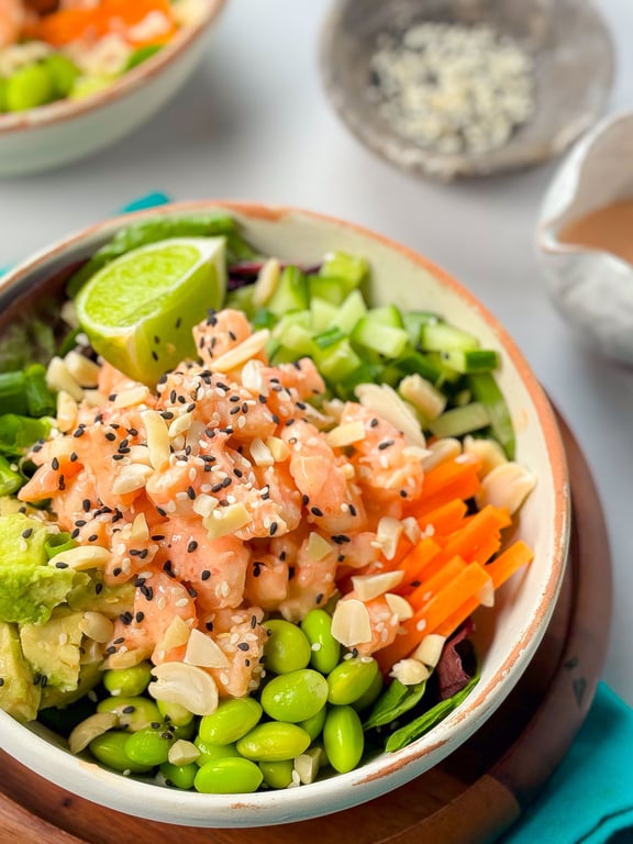 Bowl of poke with diced salmon, edamame, avocado, cucumber, carrot, lime, and sesame seeds