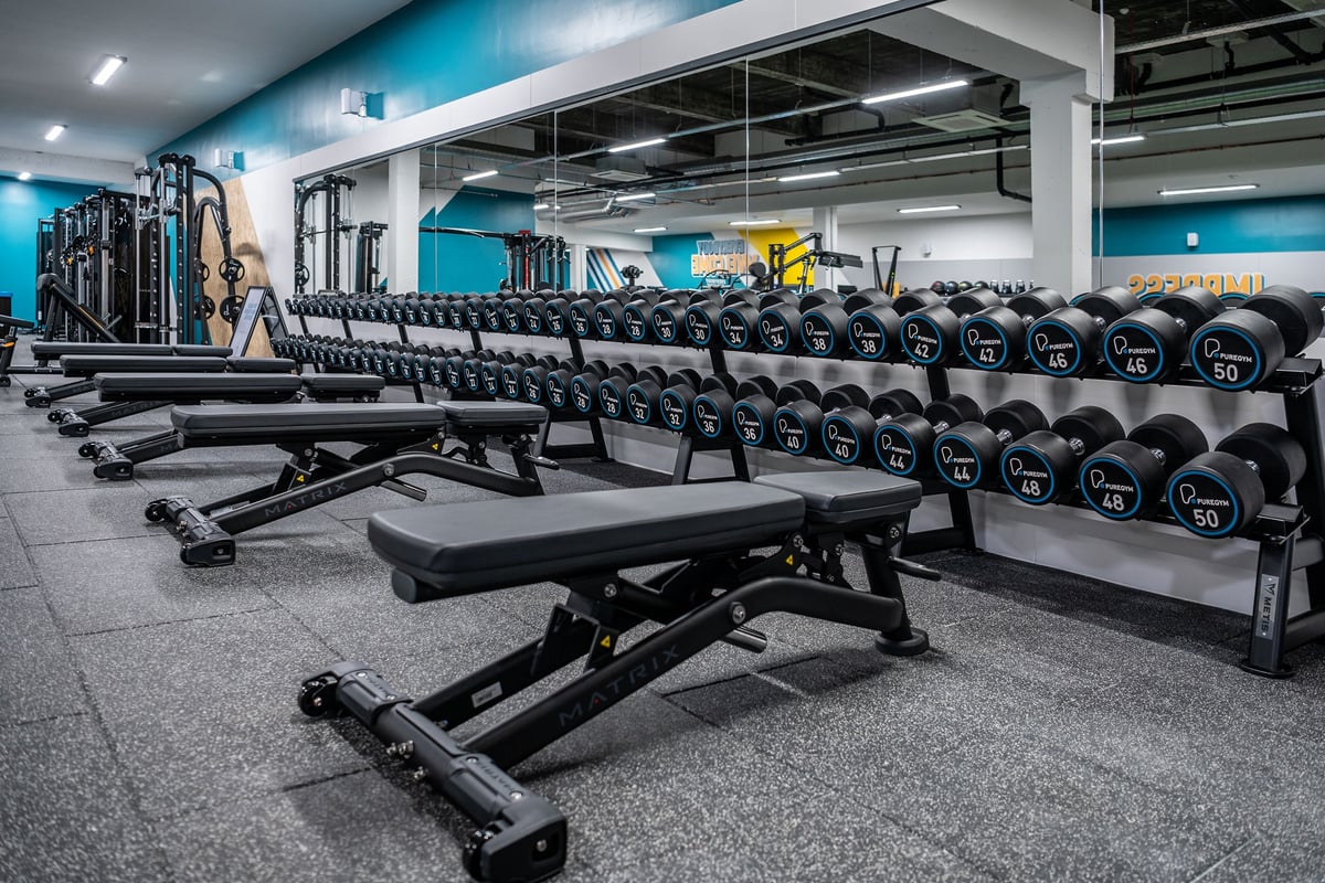 PureGym London Bethnal Green: Free weight benches, dumbbell racks, rubberized floors in a modern weight training area.