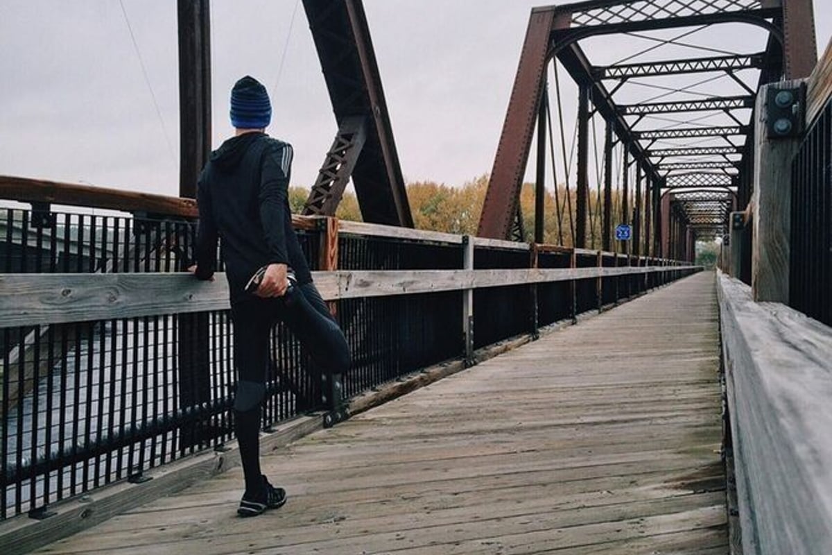 Personne en tenue de sport étirant la jambe sur un pont en bois par temps nuageux
