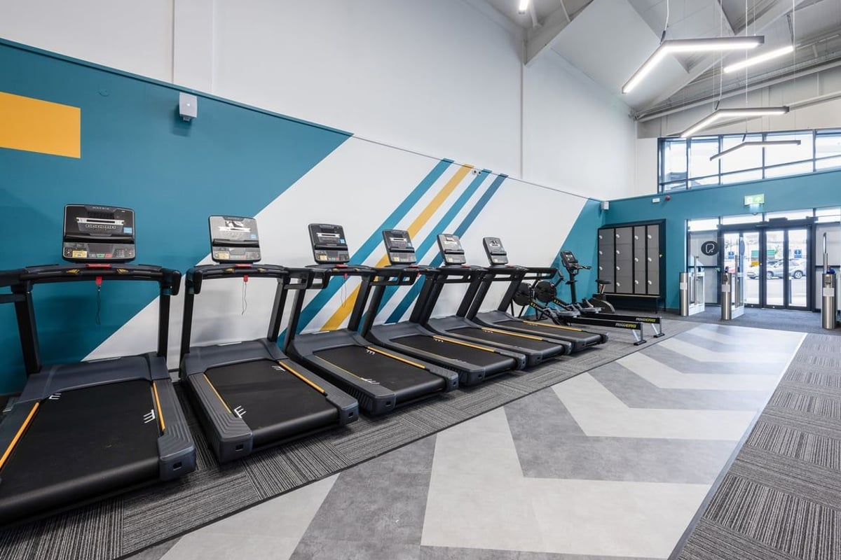 PureGym Falkirk: Rows of treadmills and other cardio machines in a brightly coloured fitness studio.