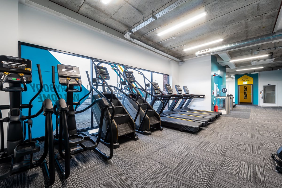 PureGym Brentwood: Rows of treadmills, ellipticals, exercise bikes in a dimly lit weightlifting area.