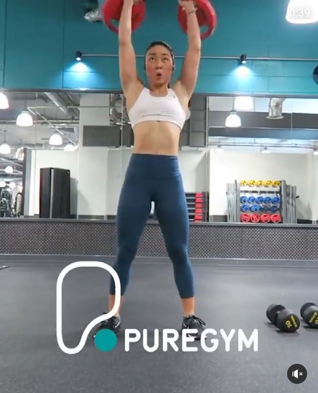 Woman lifting red weights overhead in a gym with dumbbells on the floor nearby