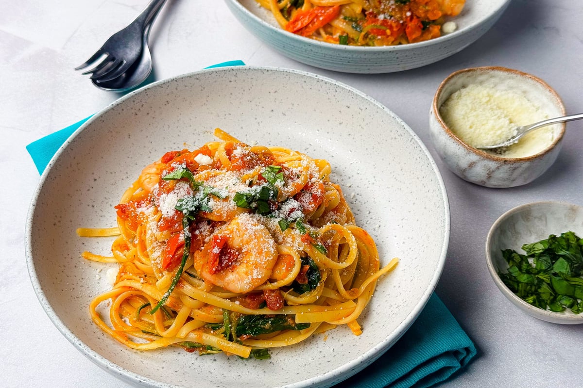 Linguine pasta with shrimp, tomato sauce, spinach, and grated cheese in bowls.