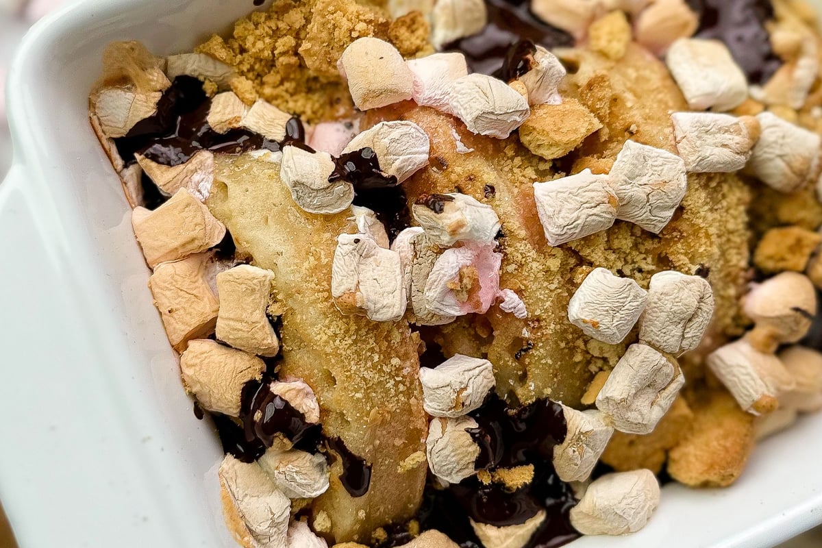 S'mores crumpets topped with marshmallows, chocolate and biscuit crumbs in white bowl