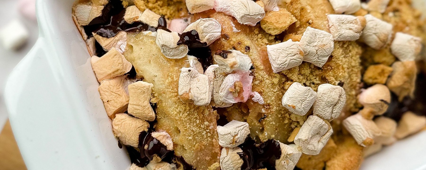 S'mores crumpets topped with marshmallows, chocolate and biscuit crumbs in white bowl