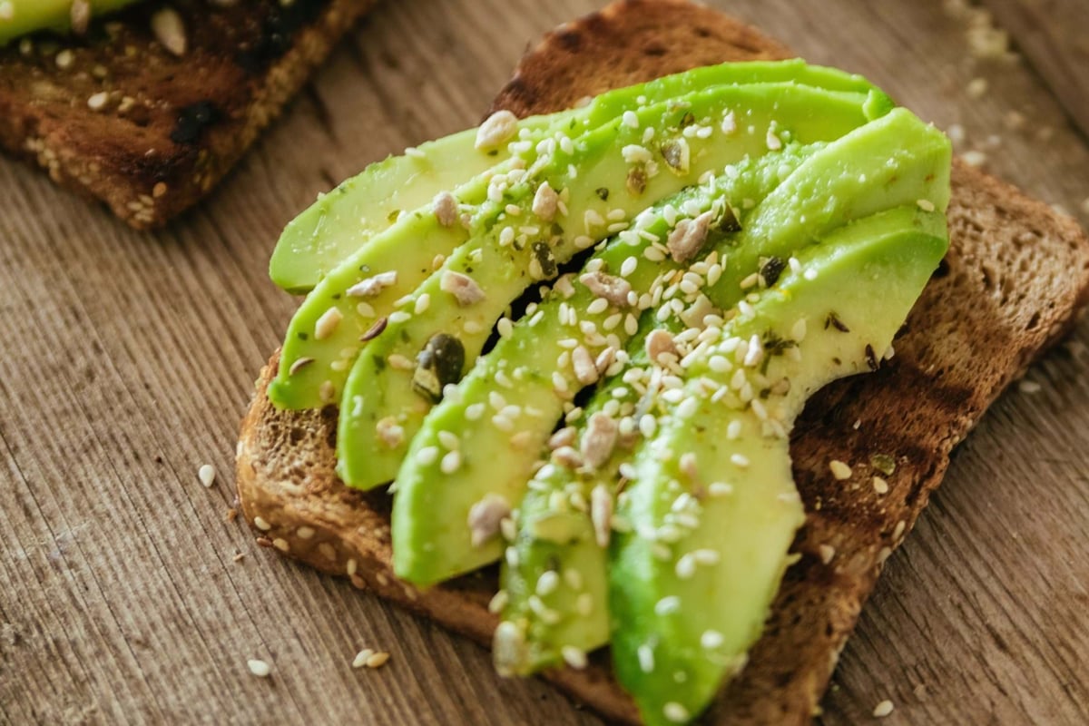 Sliced avocado with seeds on toasted whole grain bread on wooden surface