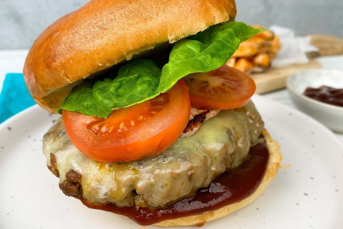 Cheeseburger with lettuce, tomato, and barbecue sauce on a white plate