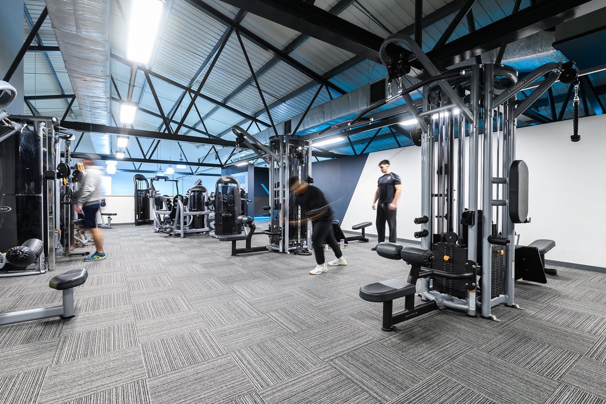 PureGym Reading Caversham Road: Gym with weight machines, benches, mirrors, and rubberized flooring under a skylight roof.