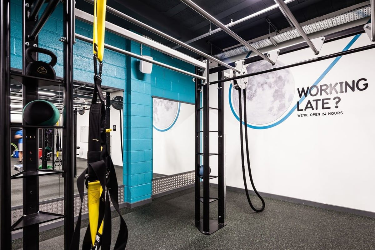 PureGym Altrincham: Resistance training rig, kettlebells, wall-mounted racks, rubberised floor, motivational signage.