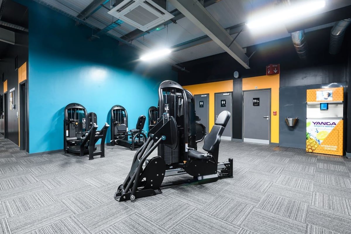 PureGym Swindon Mannington Retail Park: Weight machines, resistance equipment on rubberized flooring with blue accent wall.