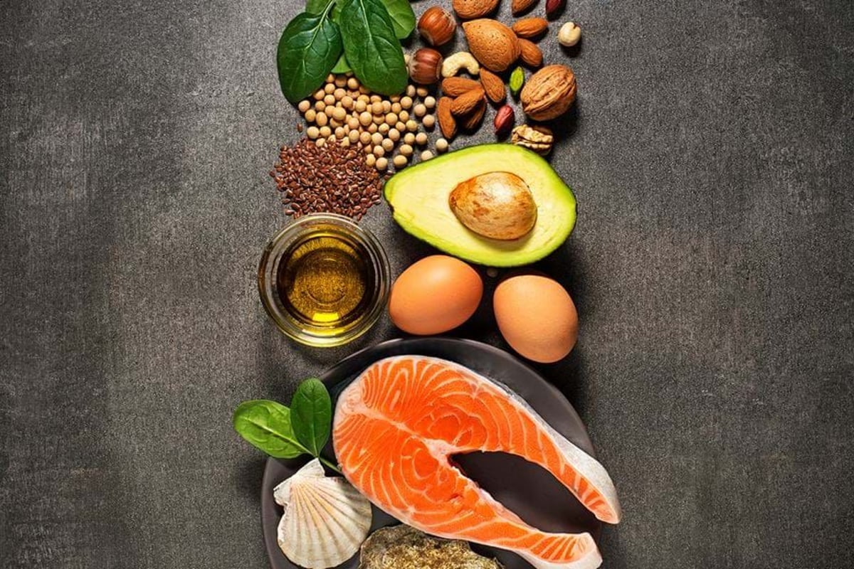 Salmon steak, avocado, eggs, nuts, seeds, spinach leaves, and oil on dark surface.