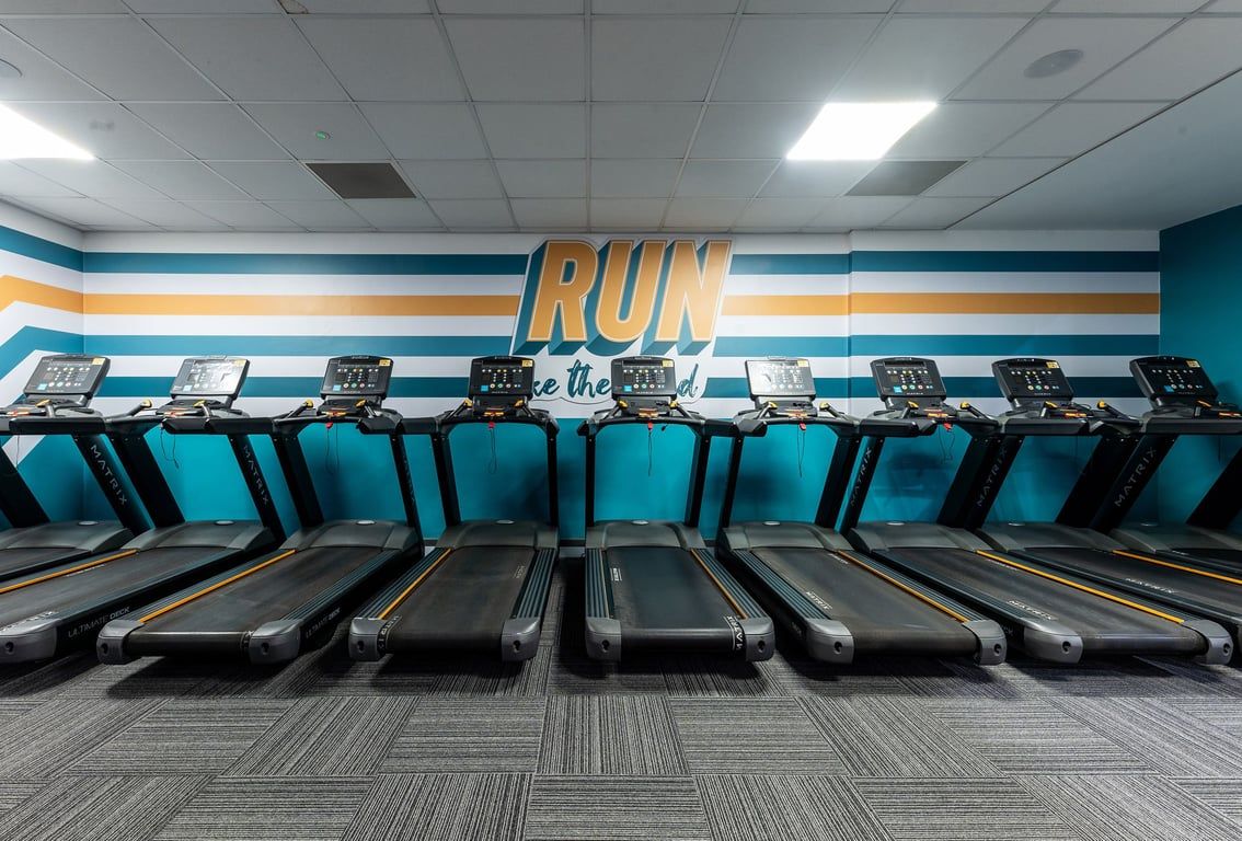 PureGym Purley: Rows of treadmills inside a brightly lit room with colourful wall branding.