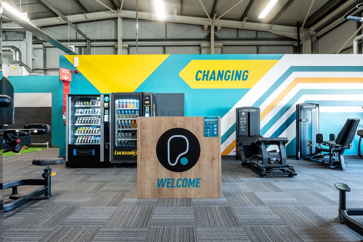 PureGym Stamford: Vending machines, exercise equipment, branded changing room welcome area with patterned flooring.