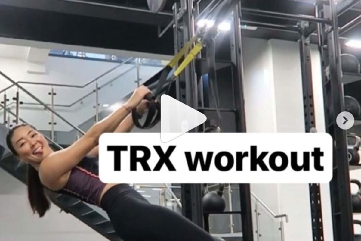 Woman doing TRX workout in gym with stairs and exercise equipment in background