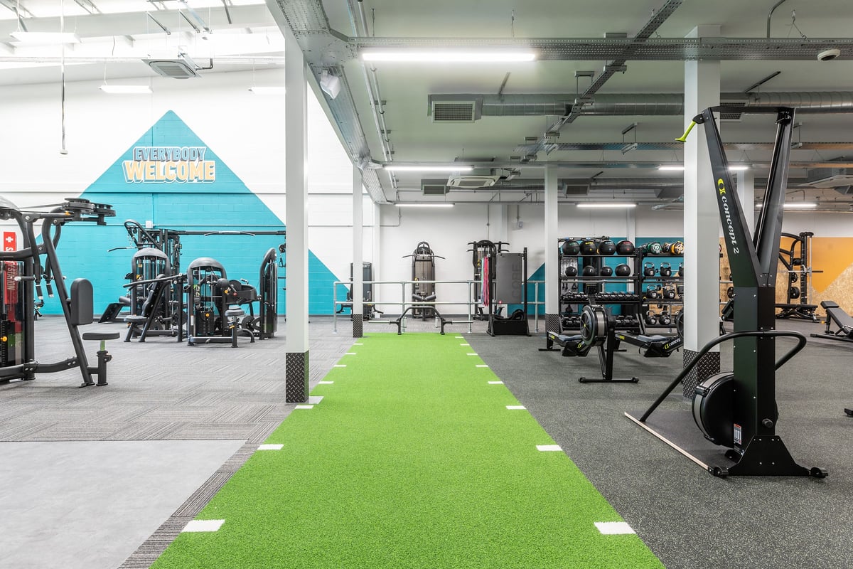 PureGym Ormskirk: Weightlifting platforms, resistance machines, green turf area, and free weight racks in a spacious gym.