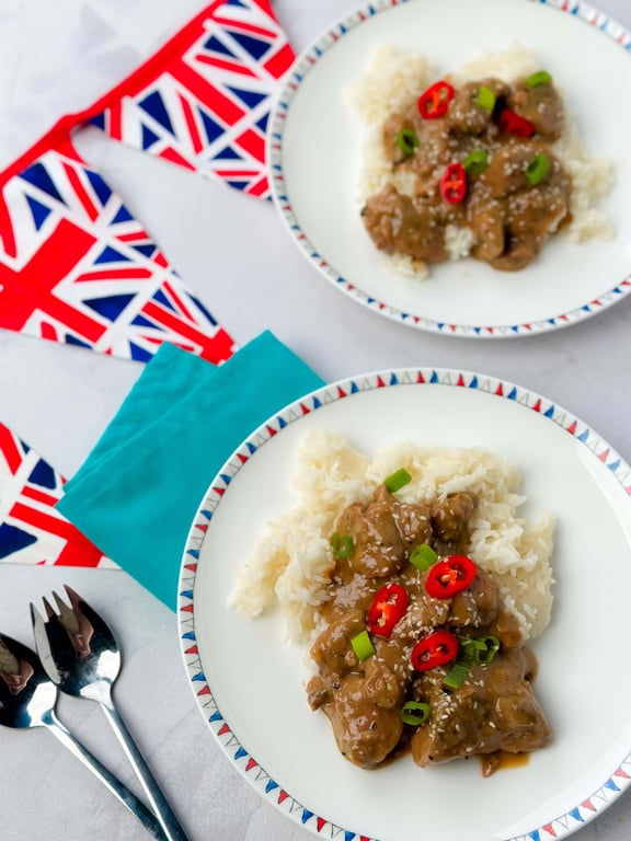 Two plates of rice with meat in sauce garnished with red chili and spring onions