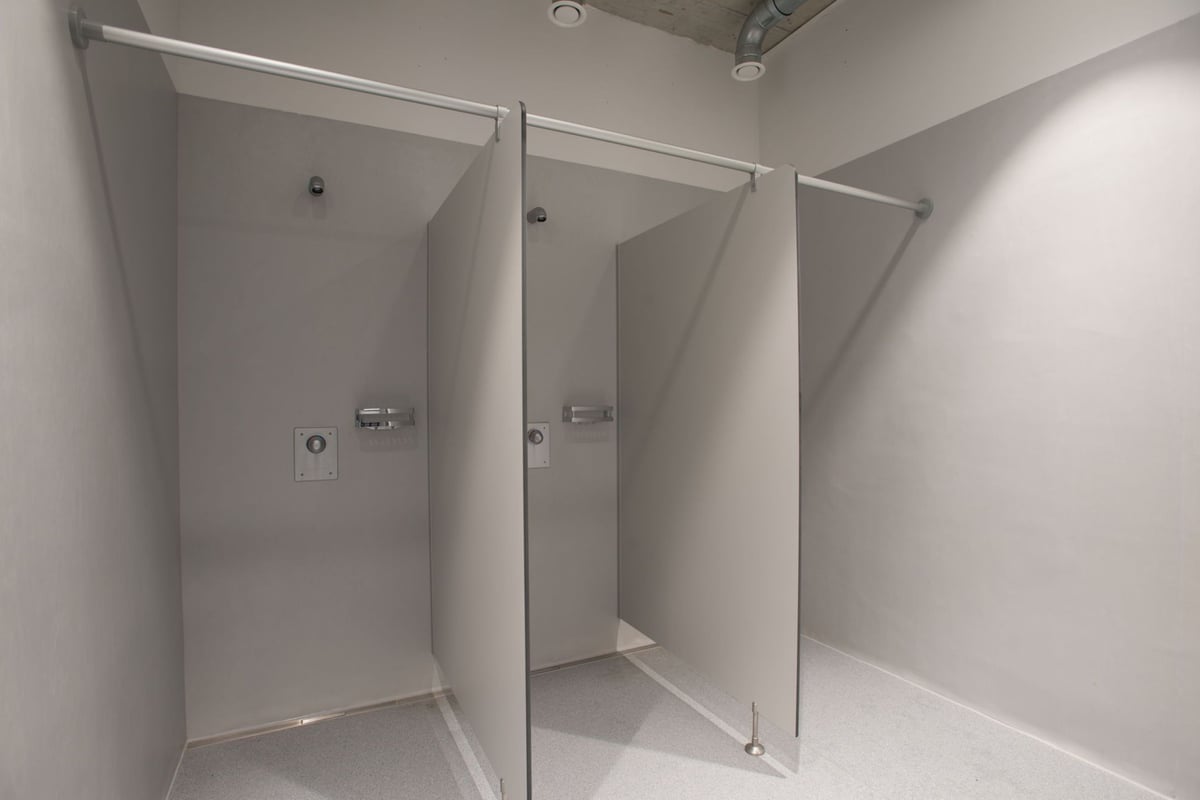PureGym Adliswil: Des rangées de cabines de douche privées avec portes en verre dépoli et sols carrelés.