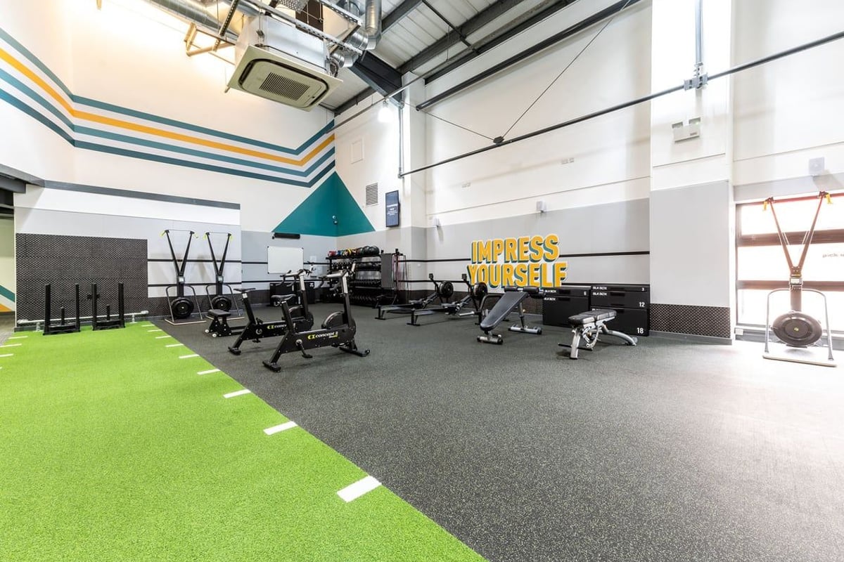 PureGym Aintree: Gym area with resistance machines, free weights, benches, green turf flooring.