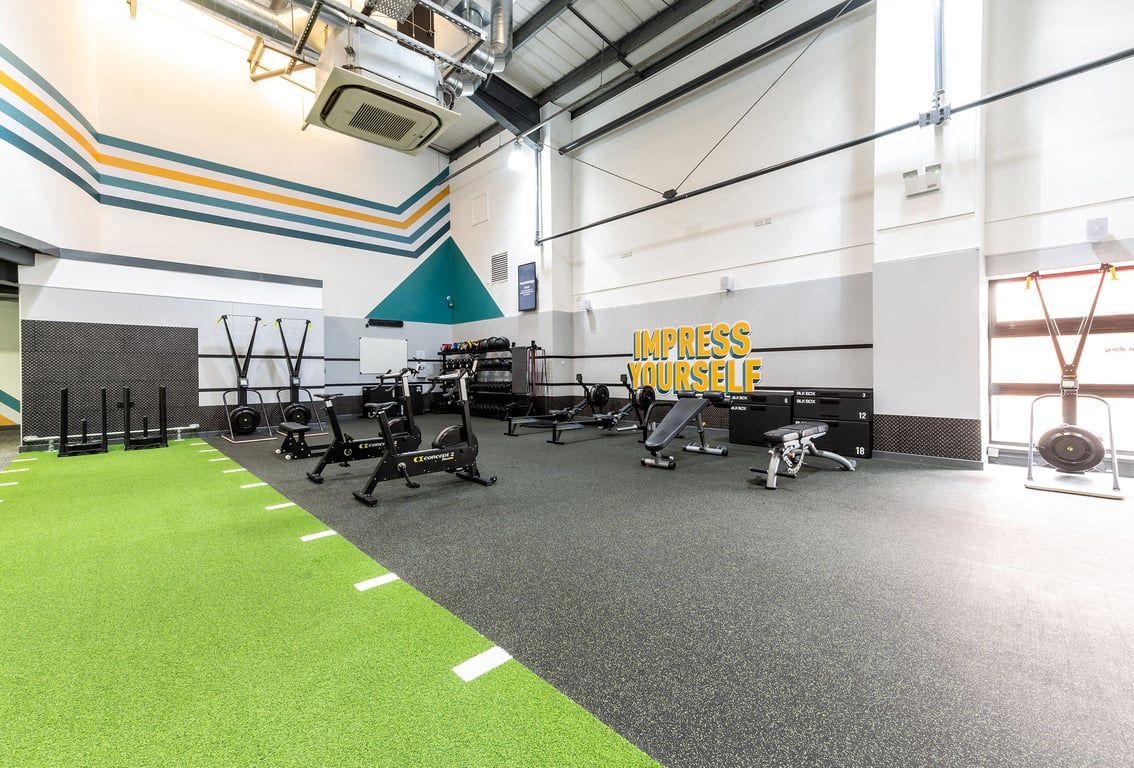 PureGym Aintree: Gym area with resistance machines, free weights, benches, green turf flooring.