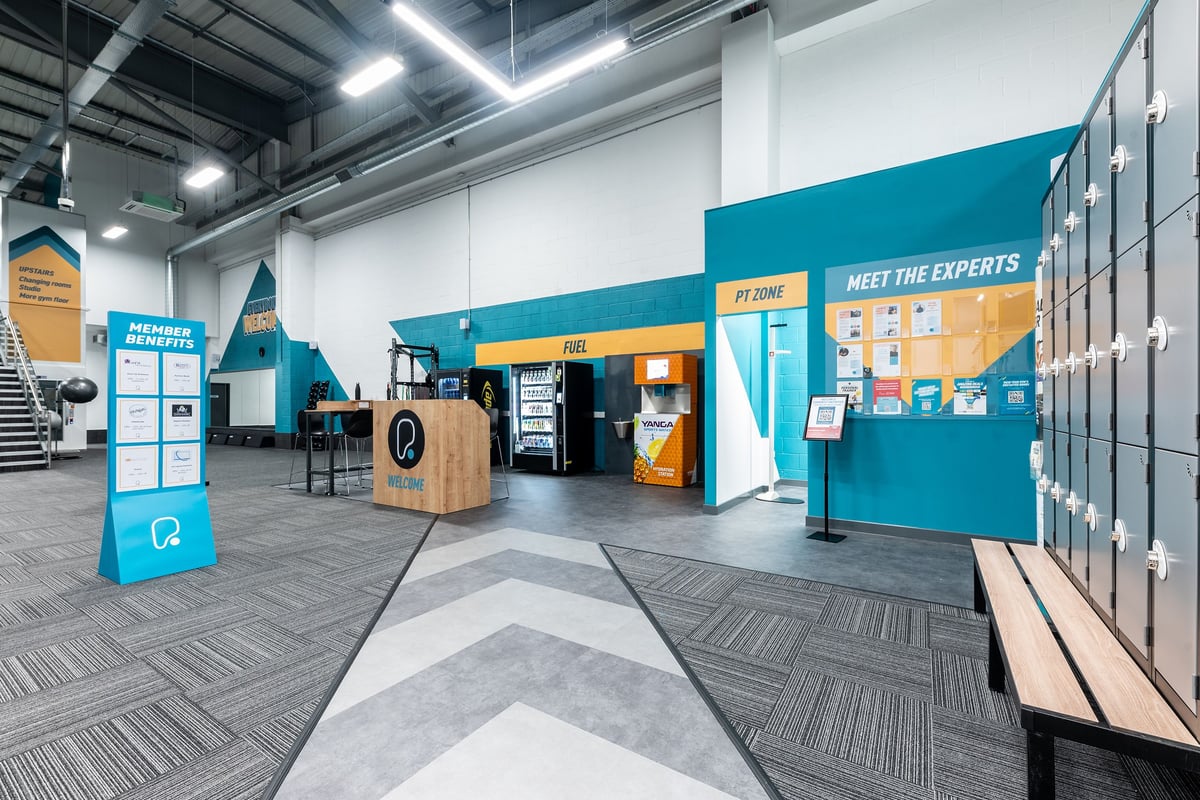 PureGym Watford Waterfields Retail Park: Welcome area with personal trainer signage, vending machines, and podium.