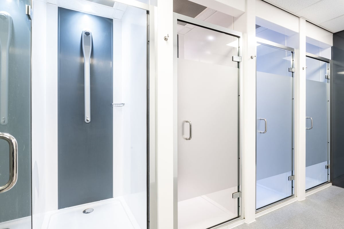 PureGym Wirral Bidston Moss: Rows of sanitized glass shower stalls or changing cubicles with metal handles.