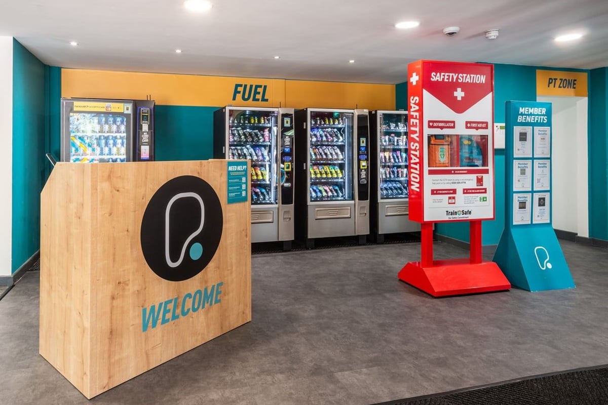 PureGym Northwich: Vending machines stocked with snacks and beverages, a safety station, and welcome signage.