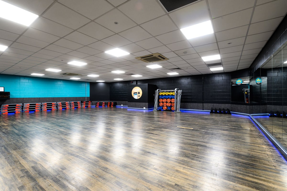 PureGym Burnham: Mirror-walled studio with exercise mats, free weights, steps, and colourful resistance bands.