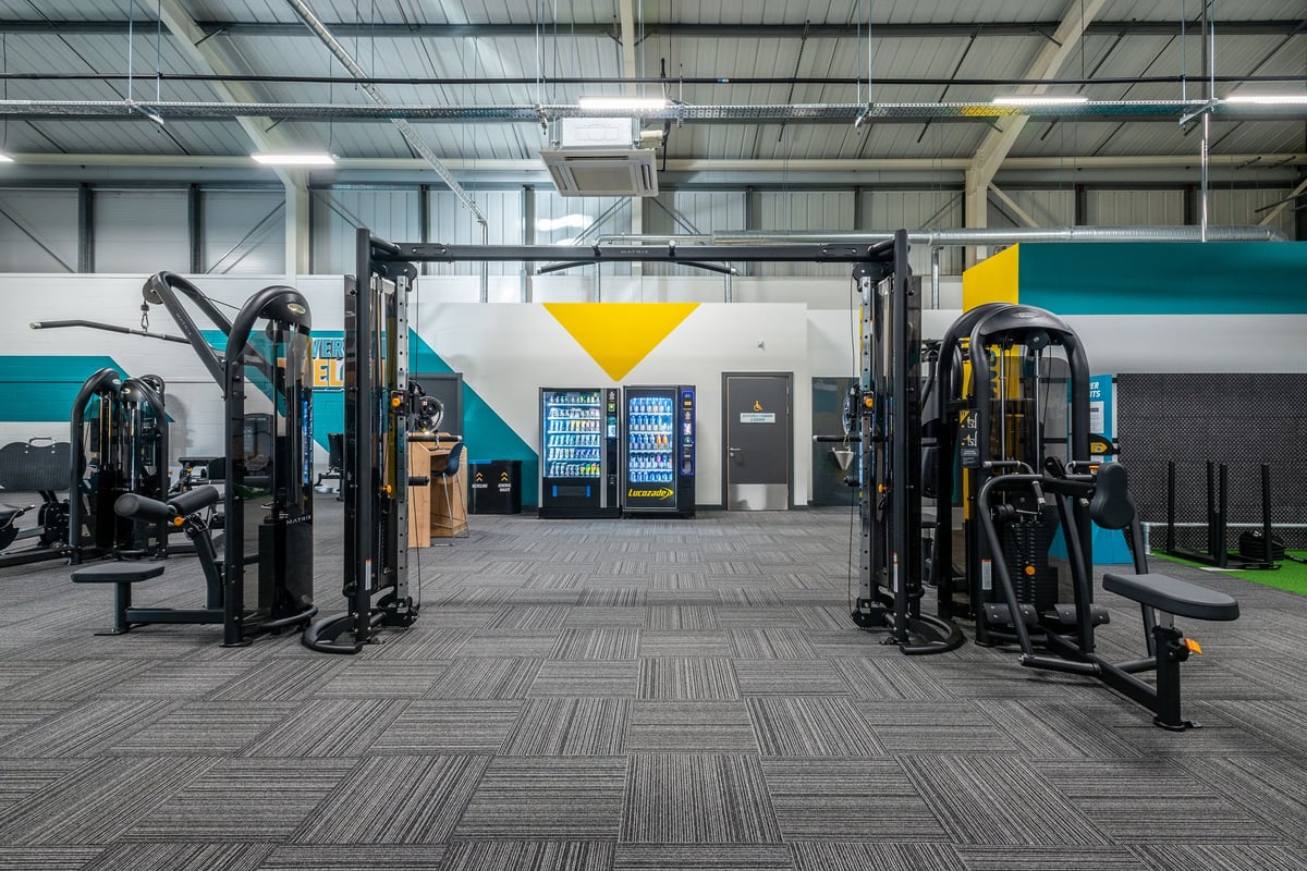 PureGym Oswestry: Gym studio with cable machines, functional trainers, rubberized flooring, and colourful accent walls.