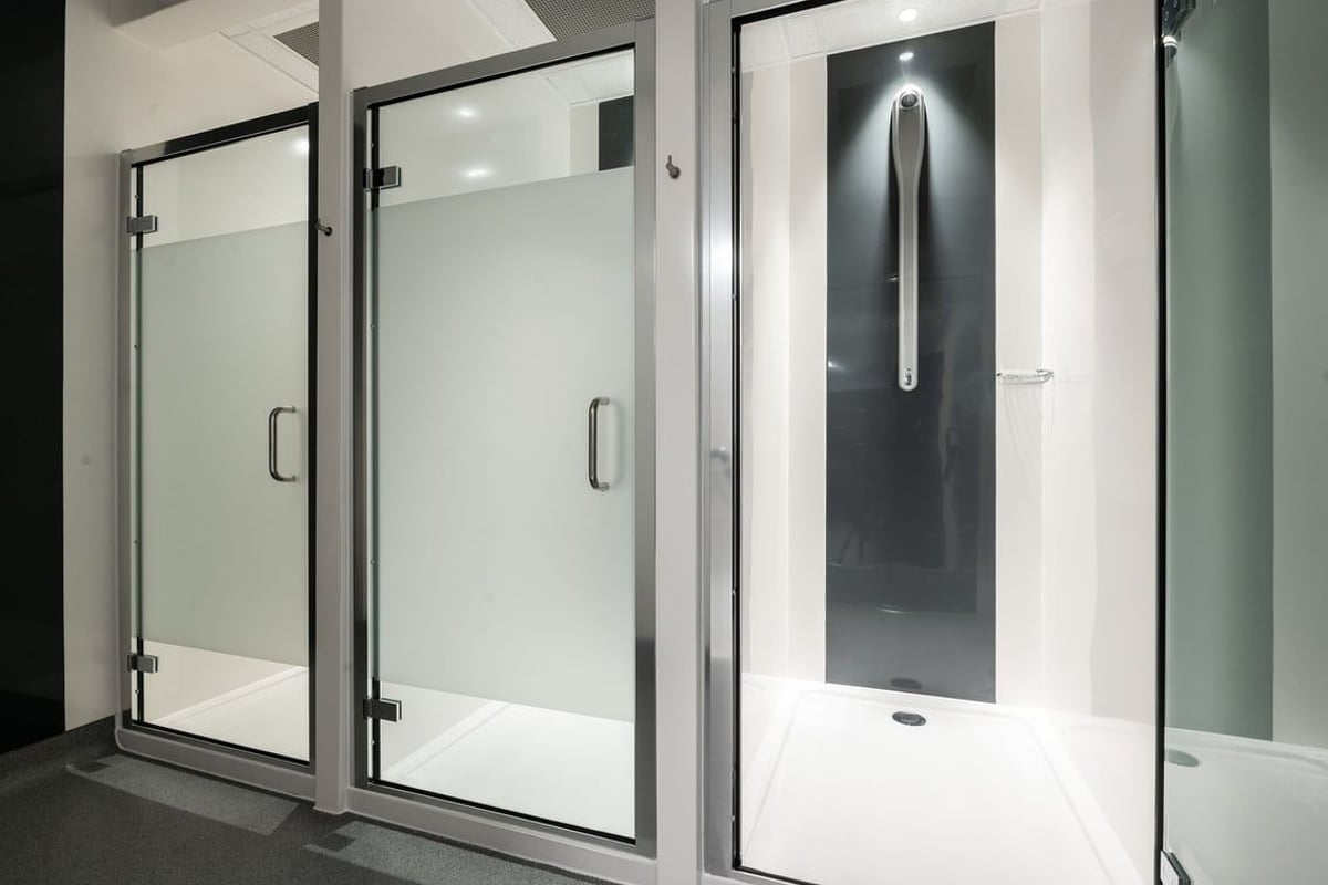 PureGym Cirencester: Shower stalls with frosted glass doors and tiled flooring.