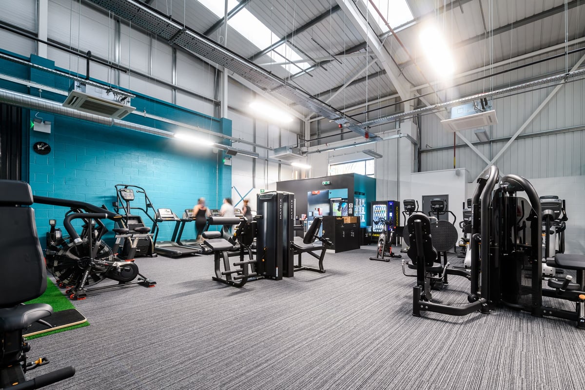 PureGym Buckingham: Weight training equipment, resistance machines, benches, and a mirrored wall in an indoor gym setting.