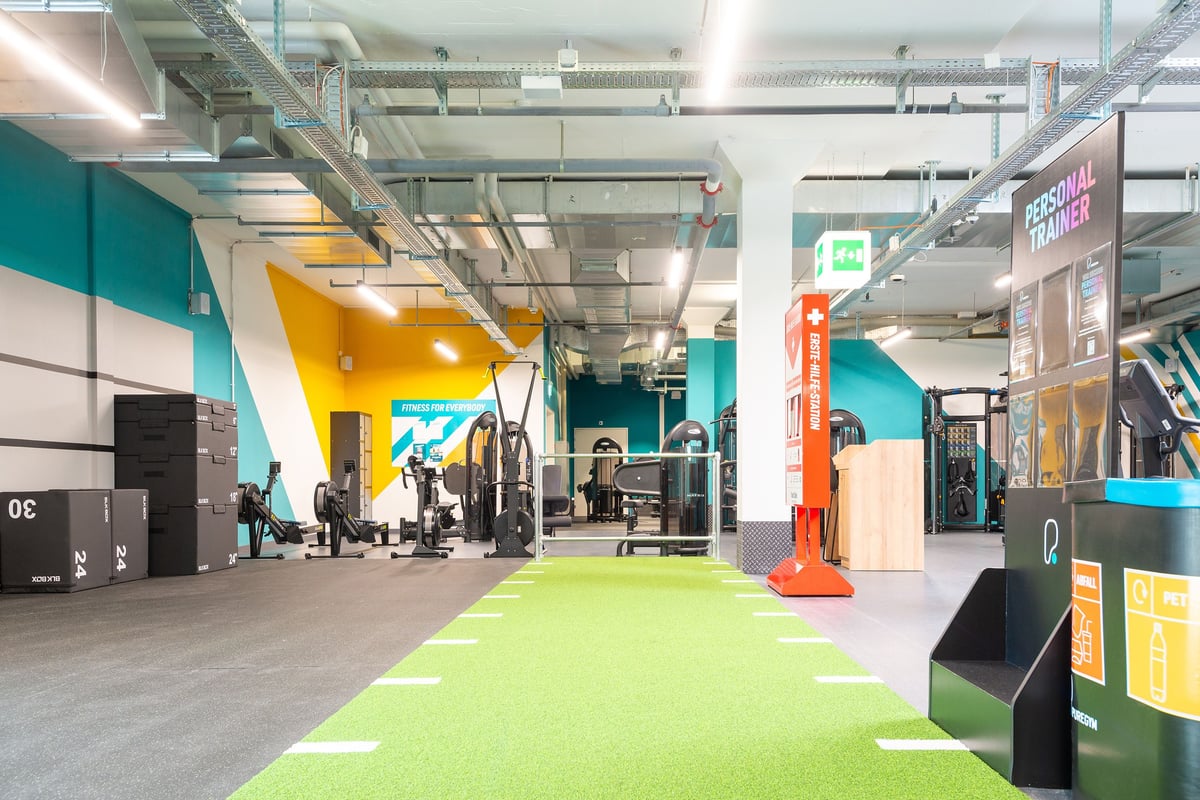 PureGym Wil: Supports de musculation, équipement d'exercice, sol en gazon et murs décoratifs éclatants.