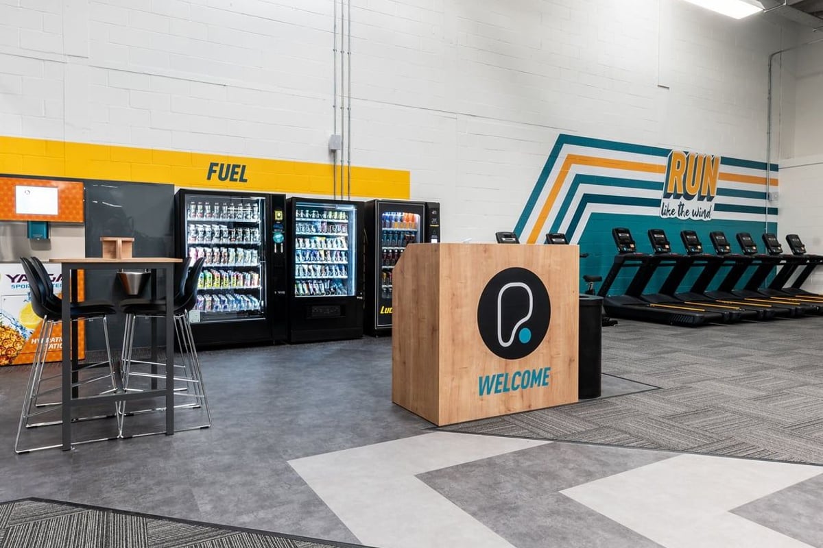 PureGym Dagenham: Rows of drink fridges, snack vending machines, a welcome desk and geometric seating area.