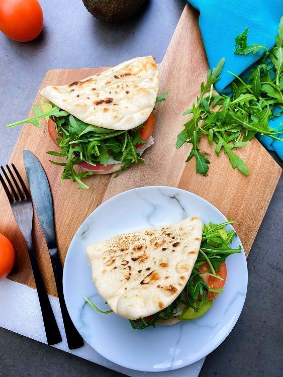 Two flatbread sandwiches with arugula and tomato on a wooden board and plate