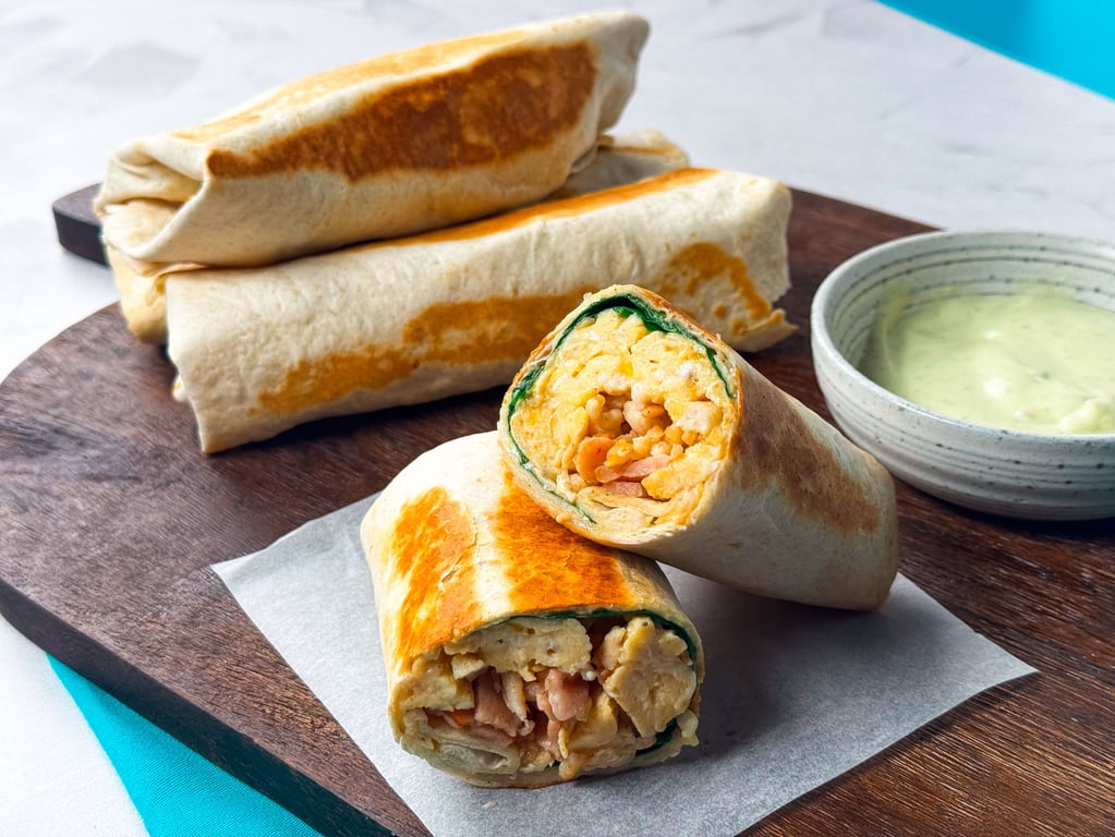 Grilled wraps filled with scrambled eggs, bacon, and spinach served with sauce.