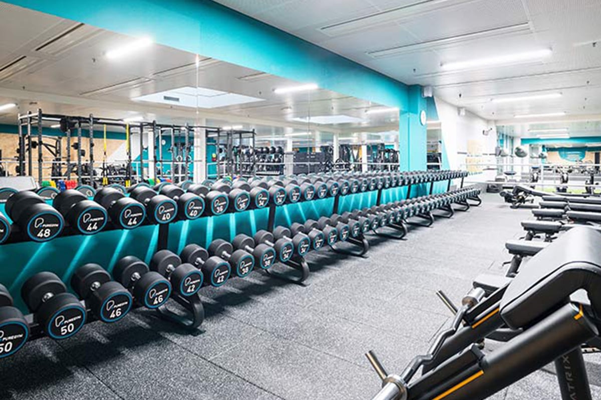 PureGym Fribourg: Des rangées d'haltères, des bancs de musculation et des appareils de résistance.