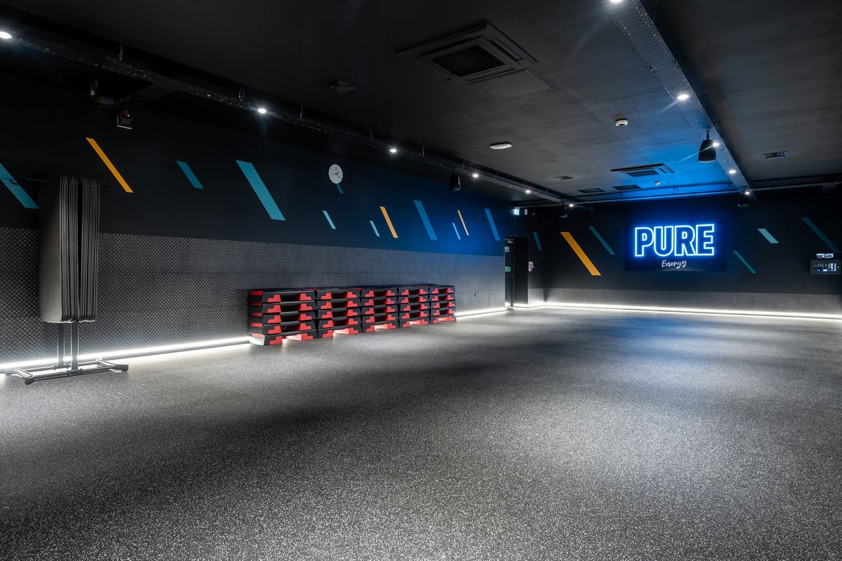 PureGym Airdrie: Rows of red spin bikes, grey walls, teal and yellow accents, mirrored Pure signage.