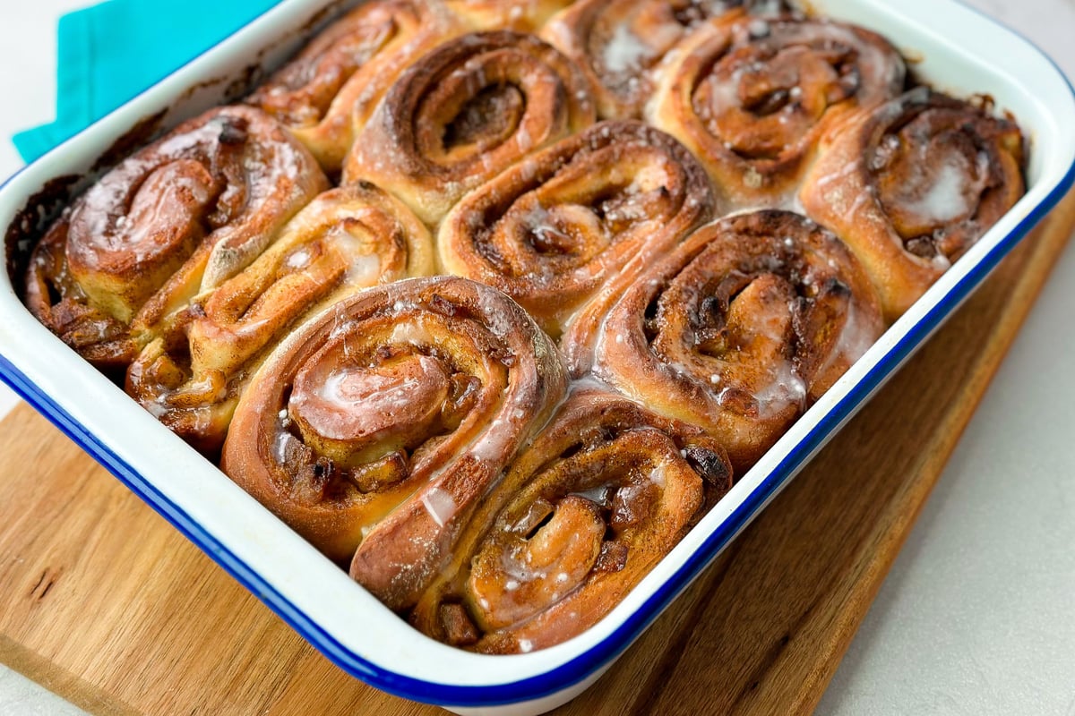 Freshly baked cinnamon rolls with toffee glaze in white enamel baking dish on wooden board