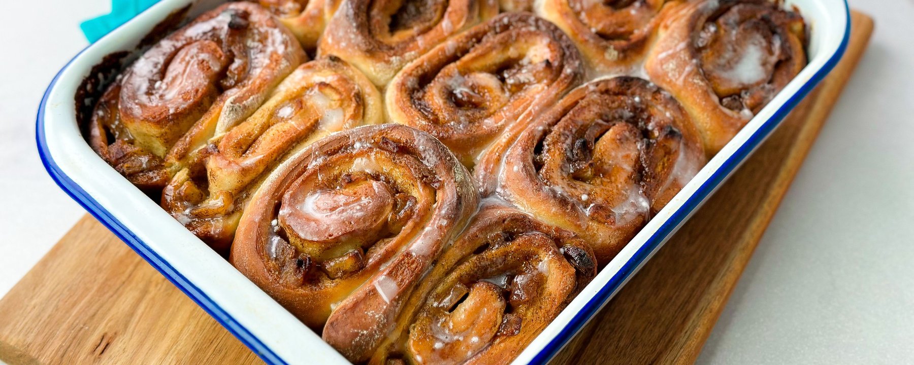 Freshly baked cinnamon rolls with toffee glaze in white enamel baking dish on wooden board