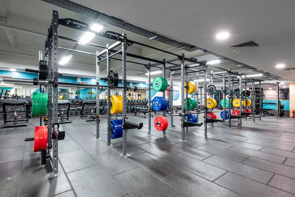 PureGym London Marylebone: Rig with multi-coloured weight plates, squat racks, rubberized flooring in a well-lit gym space.