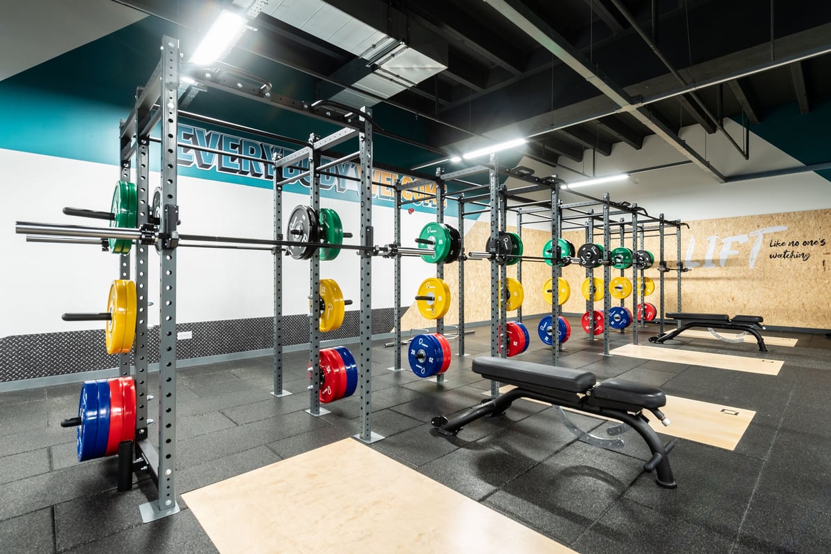 PureGym Ipswich Buttermarket: Squat racks, colourful weight plates, benches, and rubberized flooring in a weightlifting area.